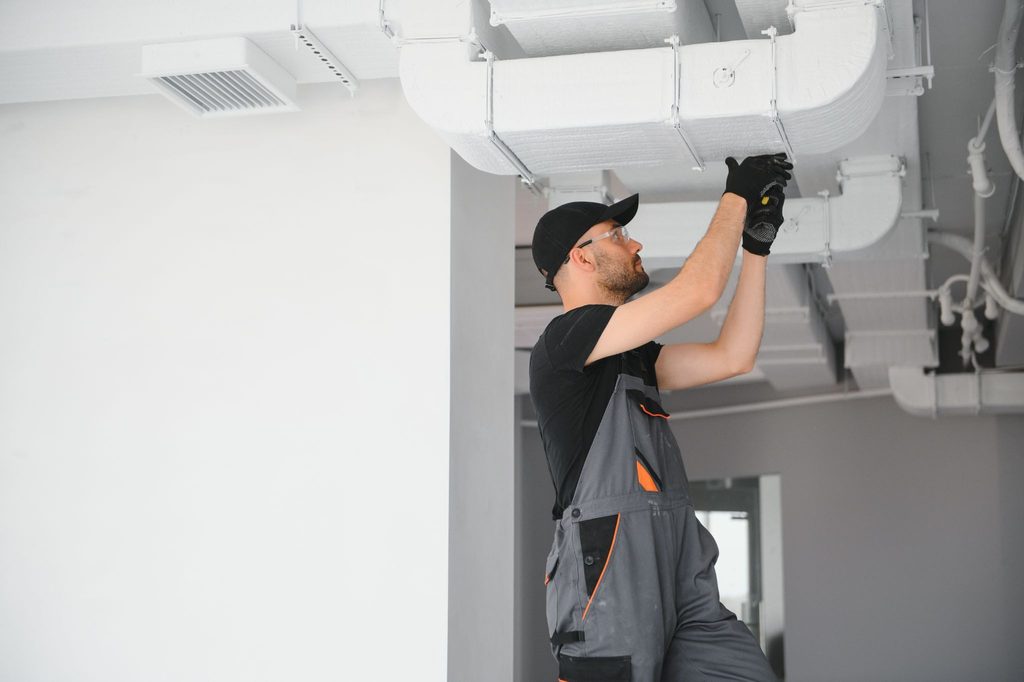 A technician in a black-and-gray uniform inspects the building ductwork before air duct cleaning